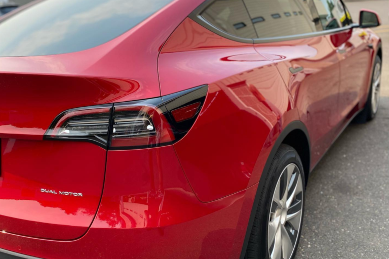 The back end of a red Tesla Model Y, emphasizing its aerodynamic shape and distinctive color.